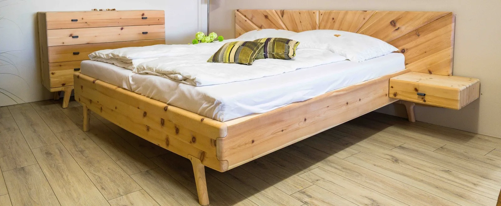 Bett aus hellem Holz mit strahlenförmigem Kopfteil, Nachtkästchen und Kommode